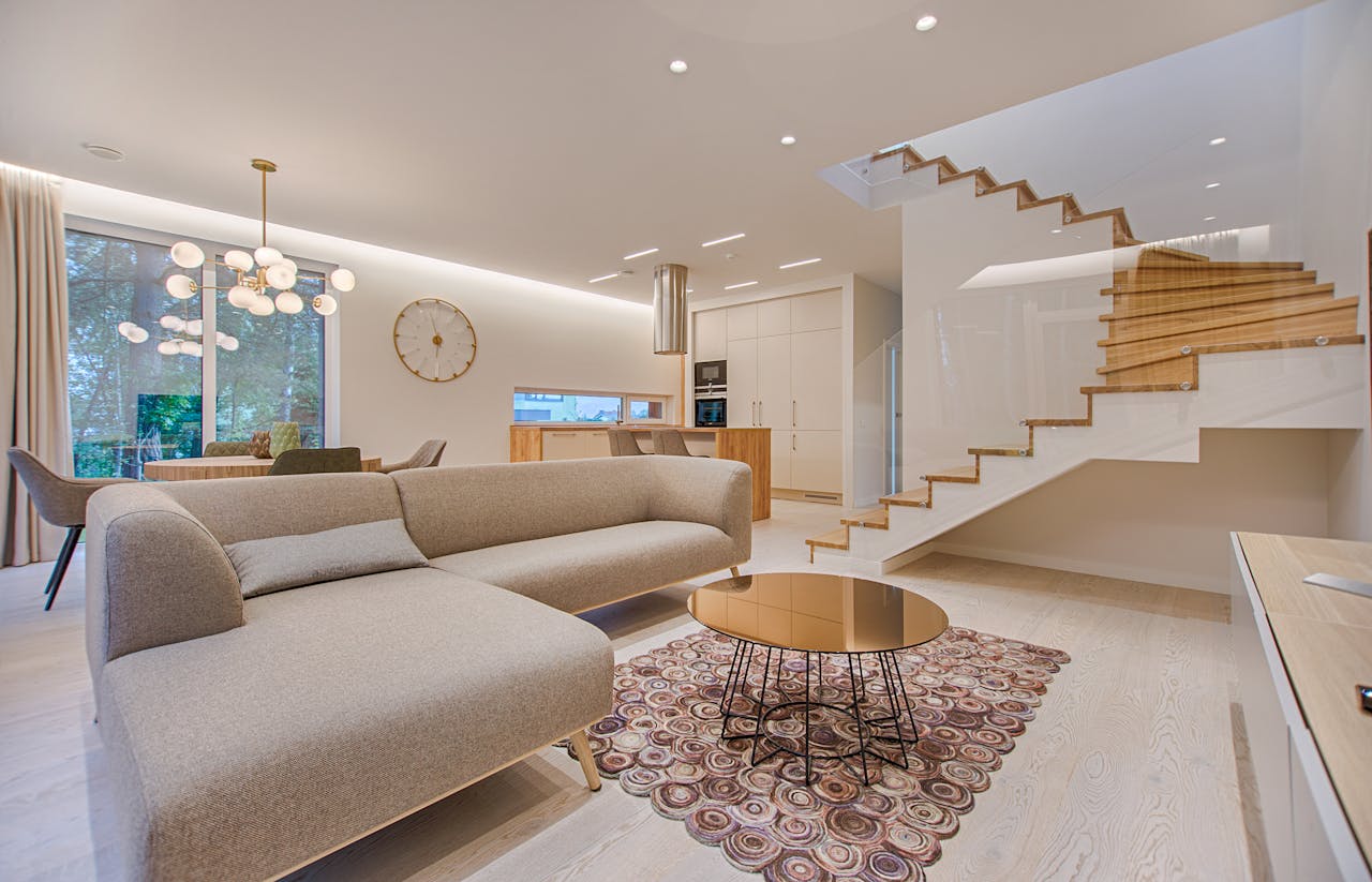 services-04 Contemporary living room with neutral tones, a sleek sofa, and elegant wooden staircase.